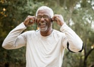 Older man smiling and adjusting headphones outside